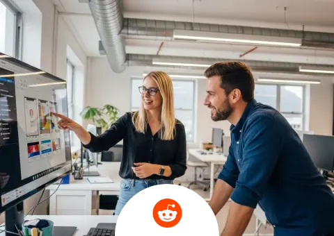 Two software developers from Tom B.'s company collaborating in a modern office, with a female developer pointing at UI charts on a large monitor for her male colleague.